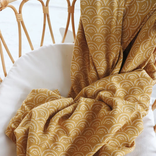 Gold patterned fabric draped over a white surface with a wicker chair in the background