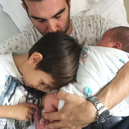 Man holding a newborn baby and a toddler, all in a hospital setting.